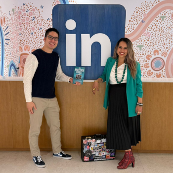 Two people smiling in front of a LinkedIn logo wall, holding books and gifts.